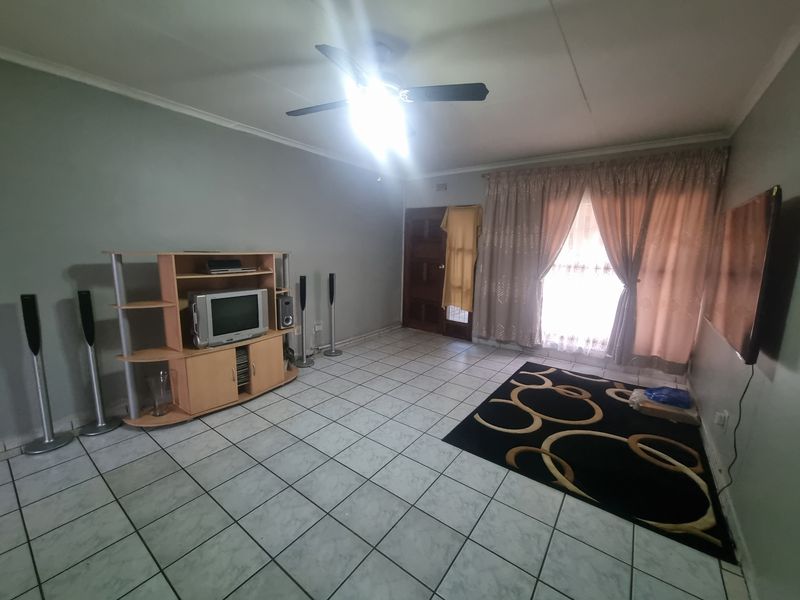 A living room featuring tiled flooring, a ceiling fan, and a sliding door leading to an outdoor area.