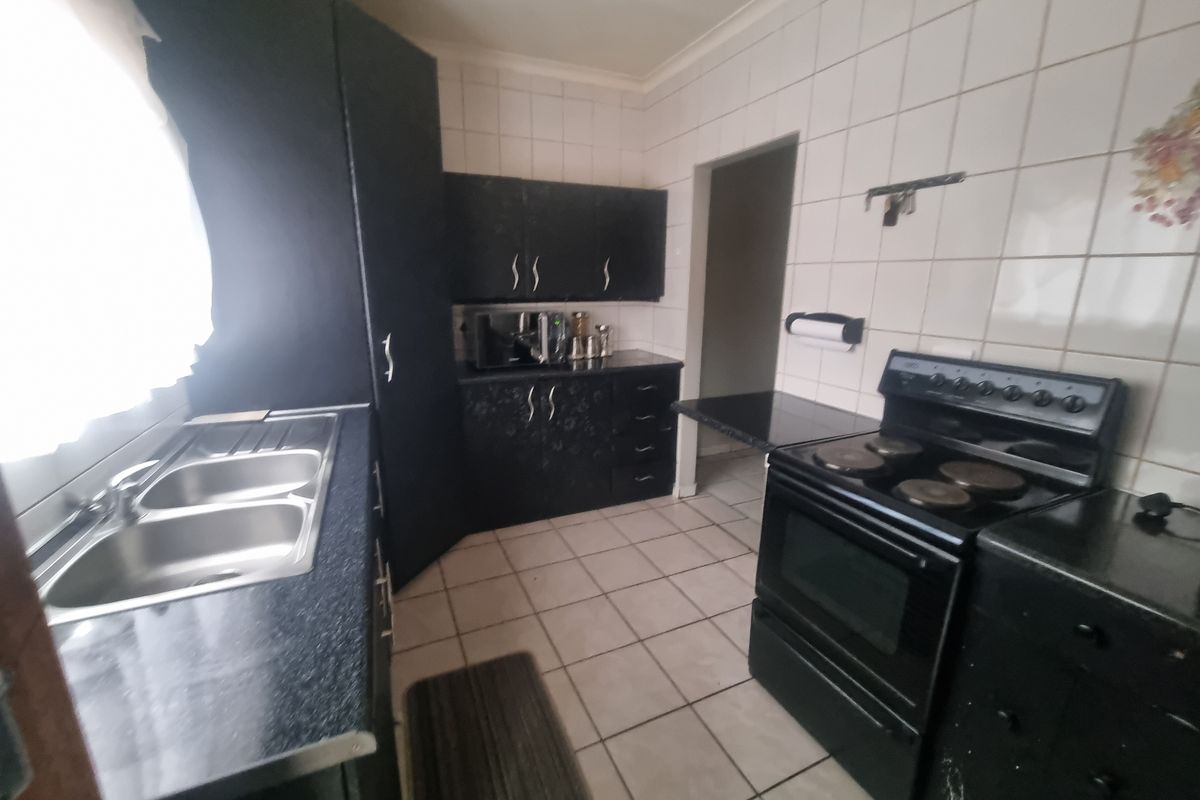 Functional kitchen featuring dark cabinetry, laminate countertops, a double bowl stainless steel sink, and a freestanding electric stove with tiled splashbacks.