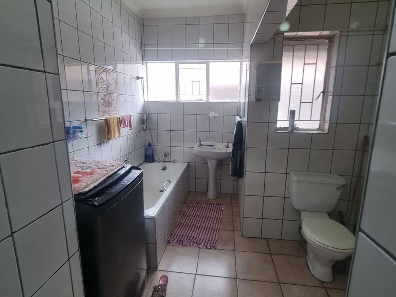 A dated bathroom featuring a pedestal basin, built-in bathtub, and toilet, finished with full-height ceramic wall tiling and floor tiles.