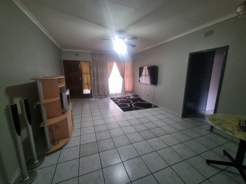 A spacious living room featuring tiled flooring, a ceiling fan, and coved cornicing, offering a functional layout for relaxation.