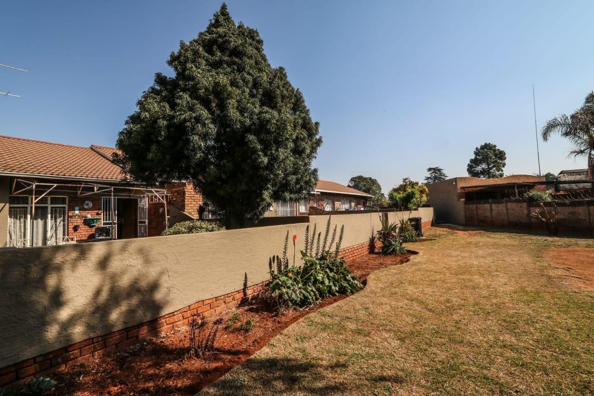 A view of the rear exterior of the apartment, featuring a private garden area, boundary wall, and tiled roof structure.