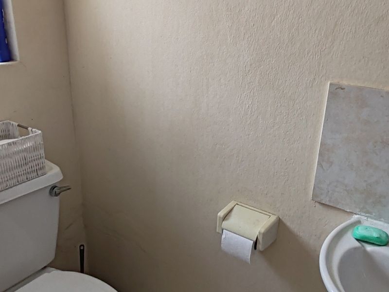 A compact bathroom featuring a standard toilet, pedestal basin, and ceramic floor tiling, requiring cosmetic updates to the wall finishes.