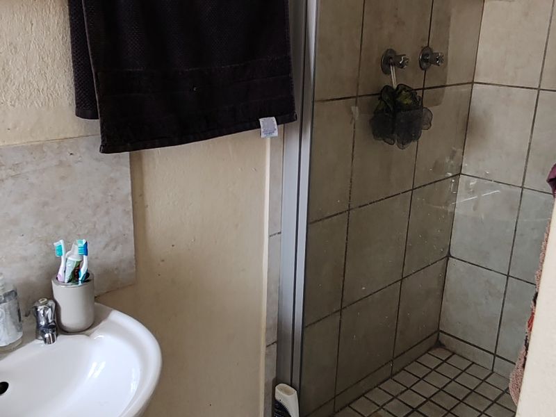 A compact bathroom featuring a pedestal basin and a glass-enclosed shower with tiled finishes, requiring some cosmetic updates to refresh the space.