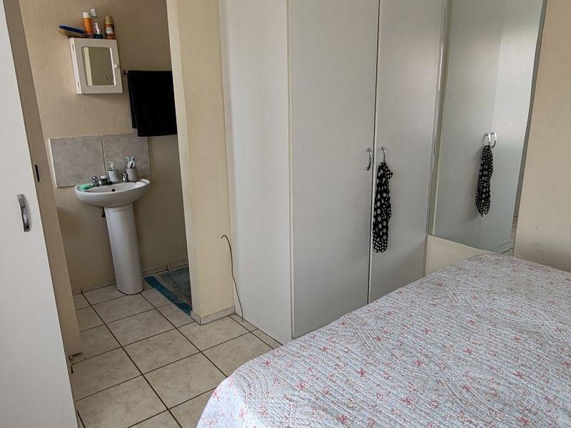 Bedroom featuring built-in wardrobes with mirrored doors and an en-suite pedestal basin area with tiled flooring.