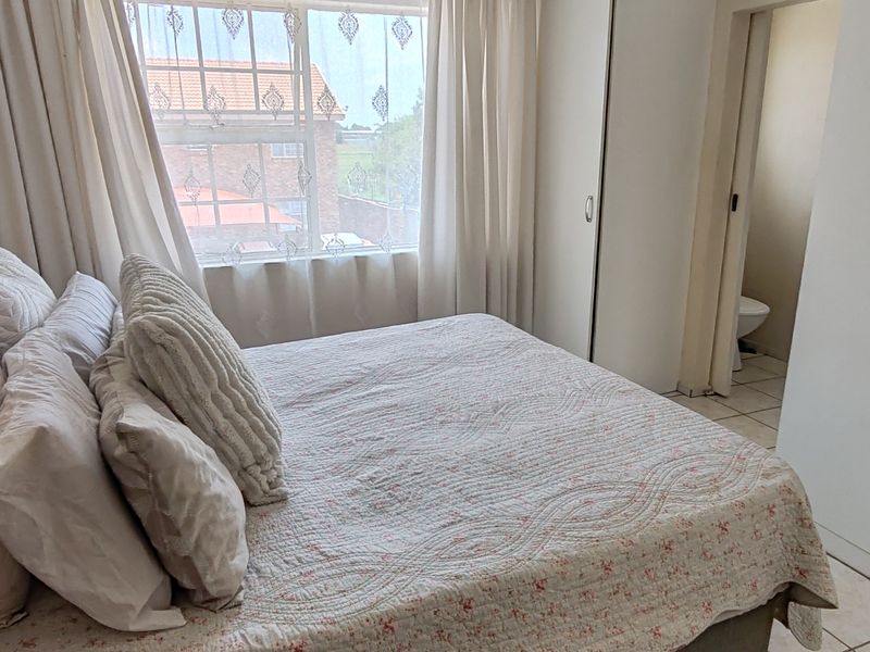 A bedroom featuring tiled flooring and built-in cupboards, with an adjacent view into a bathroom area.