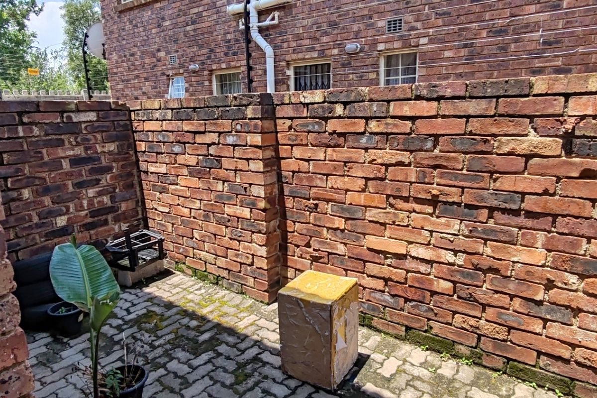 A private rear courtyard featuring exposed brick walls and paved flooring, offering a functional outdoor space for the apartment.