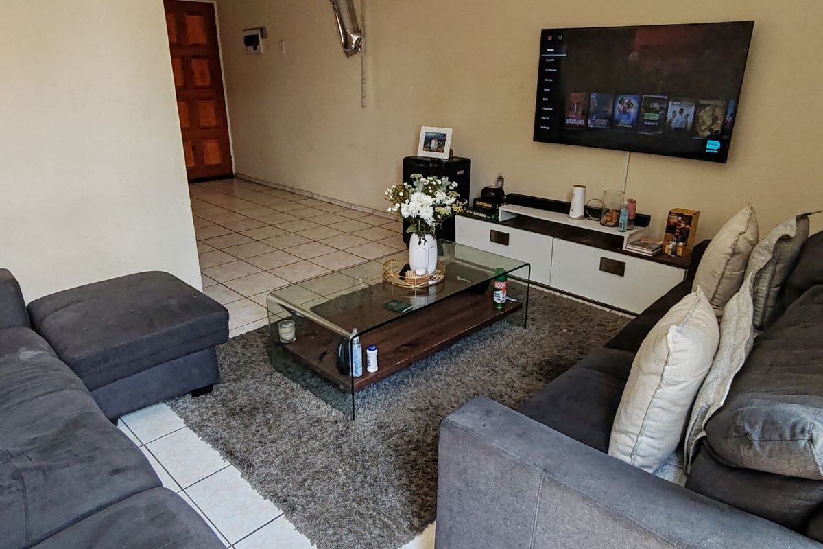 A living room area featuring tiled flooring and a wall-mounted television, providing a functional space for relaxation.