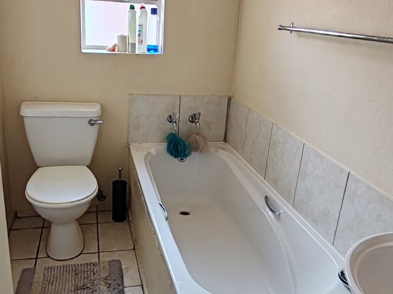 A functional bathroom featuring a standard bathtub, pedestal basin, and toilet with tiled flooring and splashbacks, requiring cosmetic updates to improve its overall condition.
