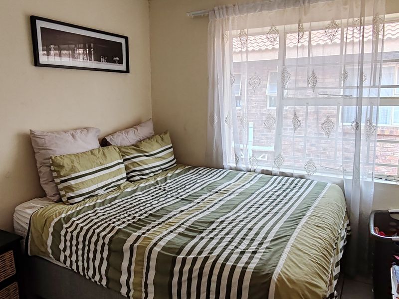 A compact bedroom featuring a window with security bars and neutral wall finishes, providing a functional space for rest.