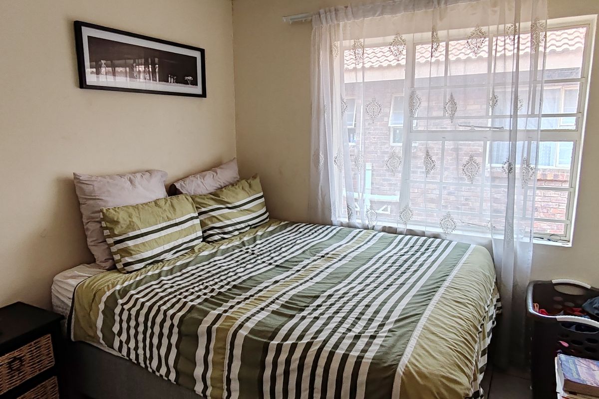 A compact bedroom featuring a window with security bars and neutral wall finishes, providing a functional space for rest.
