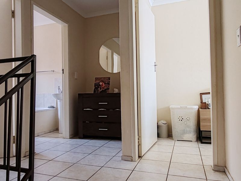 A tiled hallway area featuring a metal staircase railing, providing access to adjacent rooms including a bathroom.