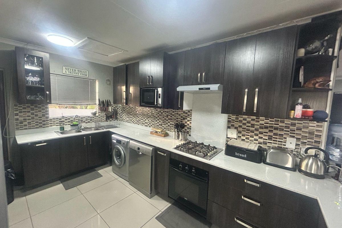 Modern kitchen featuring dark wood cabinetry, stone countertops, mosaic tile backsplash, and integrated appliances including a gas hob and built-in oven.