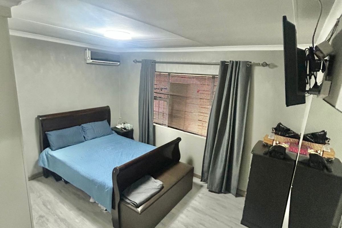 A bedroom featuring light-toned laminate flooring, a wall-mounted air conditioning unit, and window blinds.