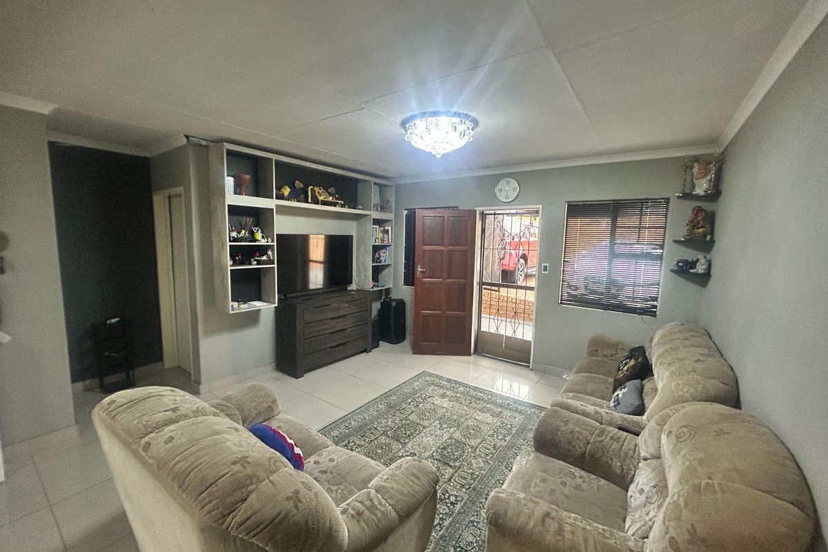 A living room featuring tiled flooring, a built-in shelving unit, and a security gate leading to the exterior.