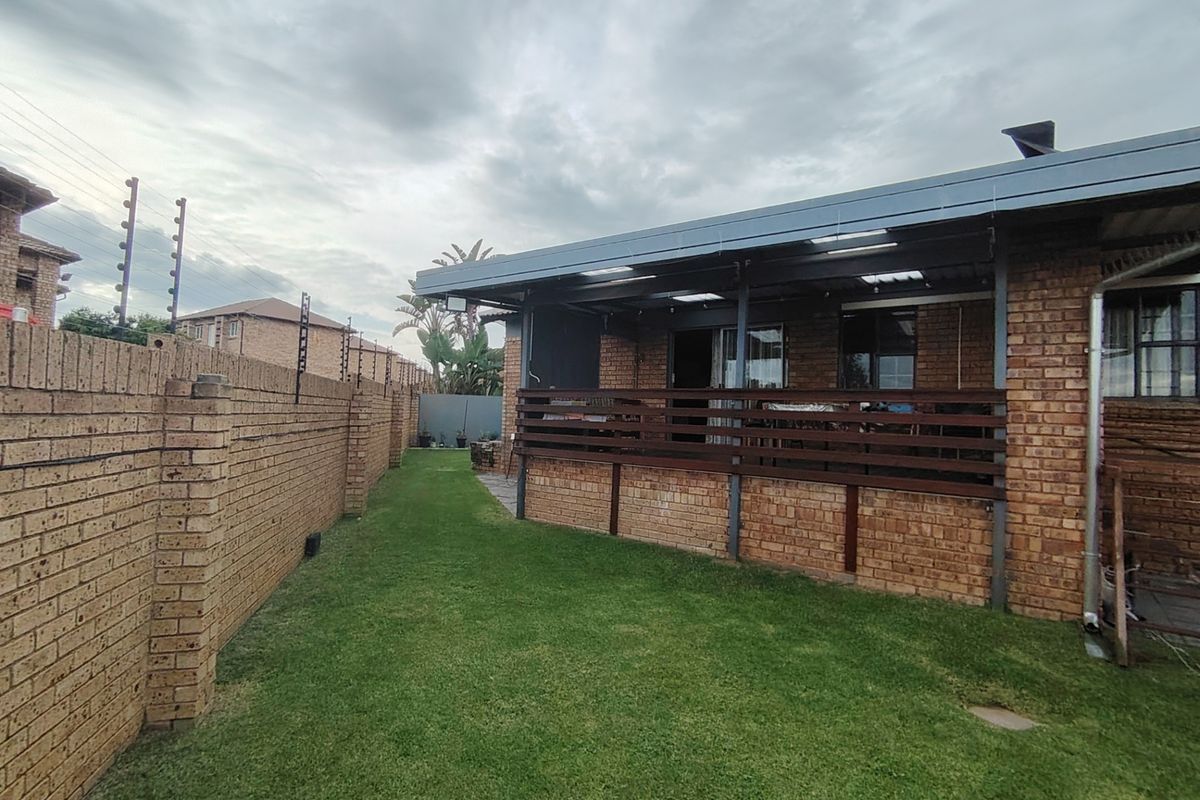 Rear view of the property featuring a brick boundary wall with electric fencing, a well-maintained lawn, and a covered patio area with timber balustrades.