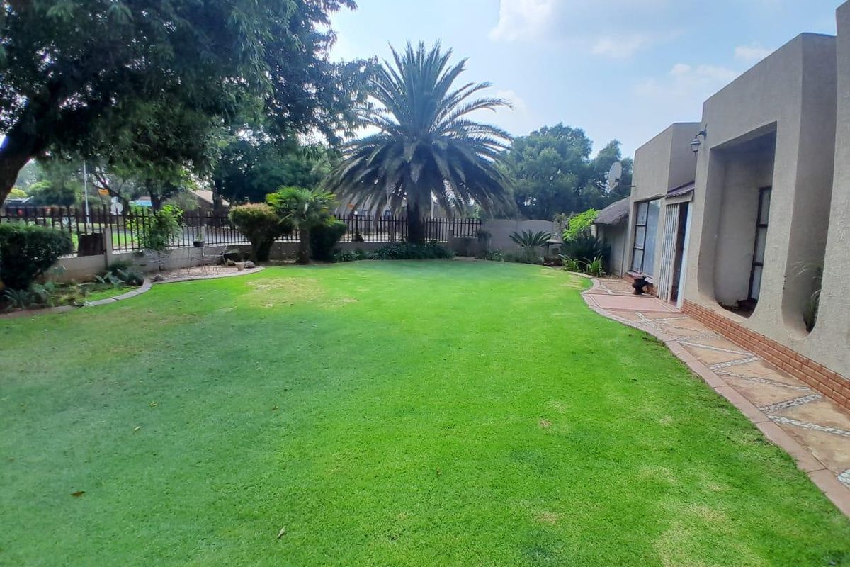 A spacious rear garden featuring a well-maintained lawn, paved walkway, and established landscaping, providing a private outdoor area adjacent to the home.
