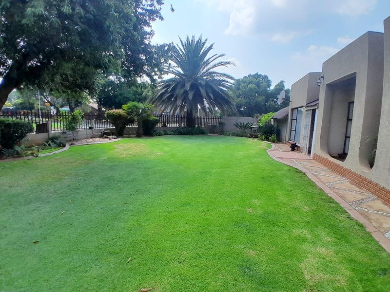 A spacious rear garden featuring a well-maintained lawn, paved walkway, and established landscaping, providing a private outdoor area adjacent to the home.