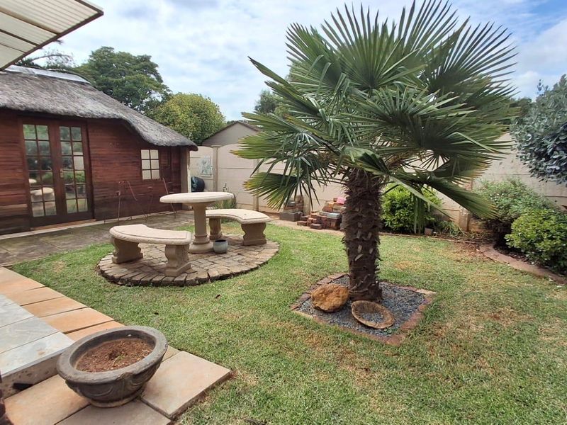 A private rear garden featuring a thatched-roof structure, paved patio area, and established landscaping, providing a tranquil outdoor space.