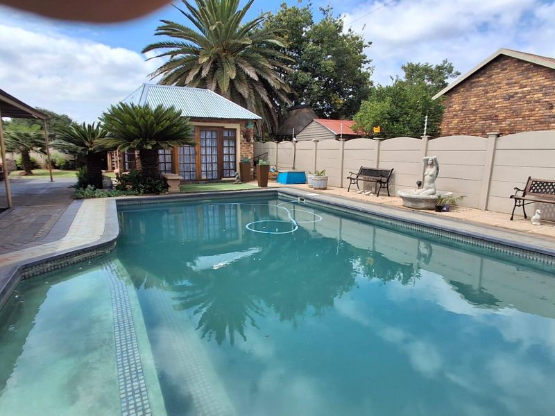 Outdoor pool area featuring a paved surround, covered patio space, and secure perimeter walling with electric fencing.