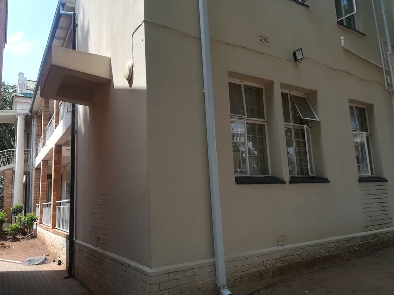 Side view of the apartment building exterior featuring painted walls, brick base detailing, and security-fitted casement windows.