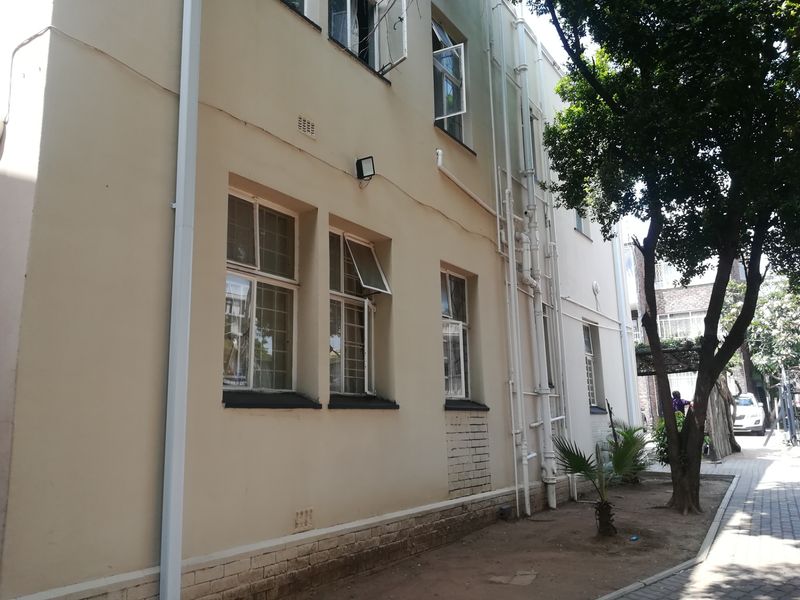 Exterior view of the apartment building rear facade, featuring steel-framed windows, exposed plumbing, and a paved walkway area.
