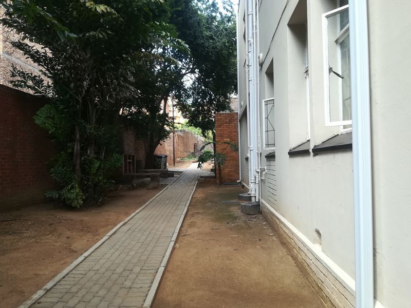 A side exterior view of the apartment building featuring a paved walkway, brick boundary walls, and external plumbing infrastructure.
