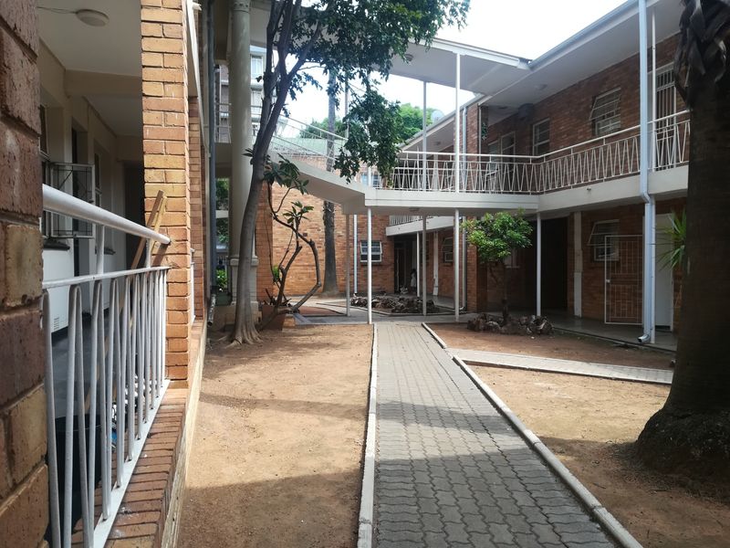 A view of the apartment complex courtyard featuring brick facades, covered walkways, and a central paved path through the garden area.