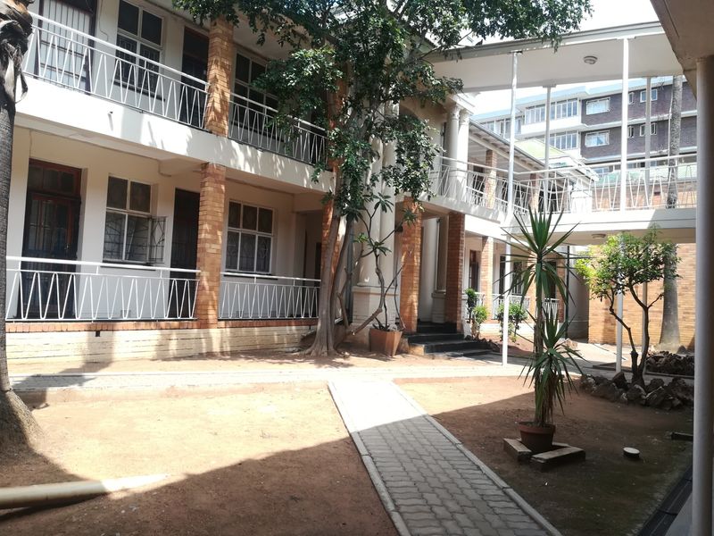 A view of the apartment complex courtyard featuring multi-story walkways, brick columns, and a paved path through the central garden area.