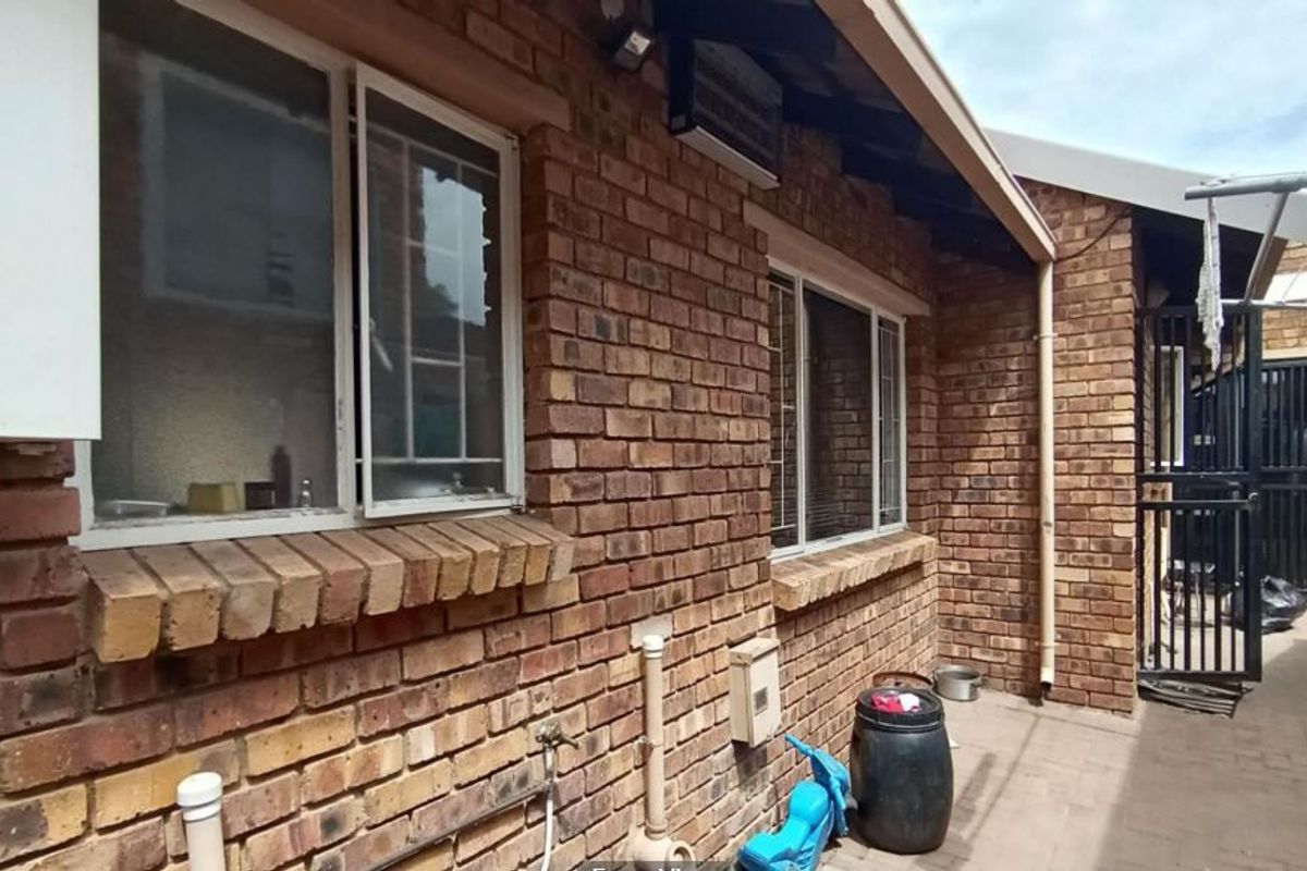 Rear exterior view of the property featuring face brick walls, a wall-mounted gas geyser, security bars on windows, and a paved side walkway.