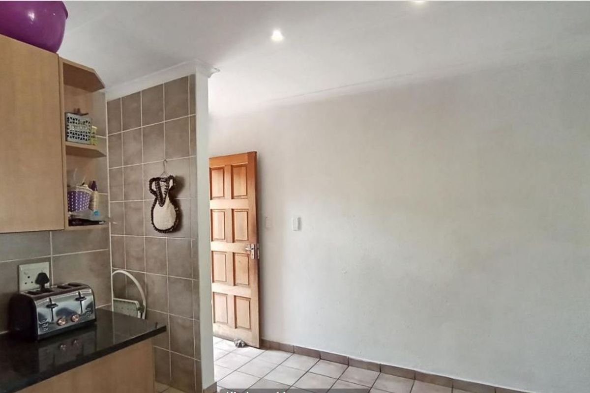 A functional kitchen area featuring laminate cabinetry, granite countertops, tiled splashbacks, and tiled flooring, with recessed downlighting and a timber door.