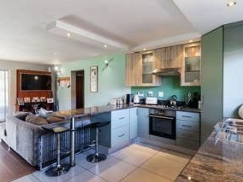 Open-plan living area featuring a modern kitchen with stone countertops, integrated oven, extractor fan, and tiled flooring, seamlessly flowing into the lounge space.