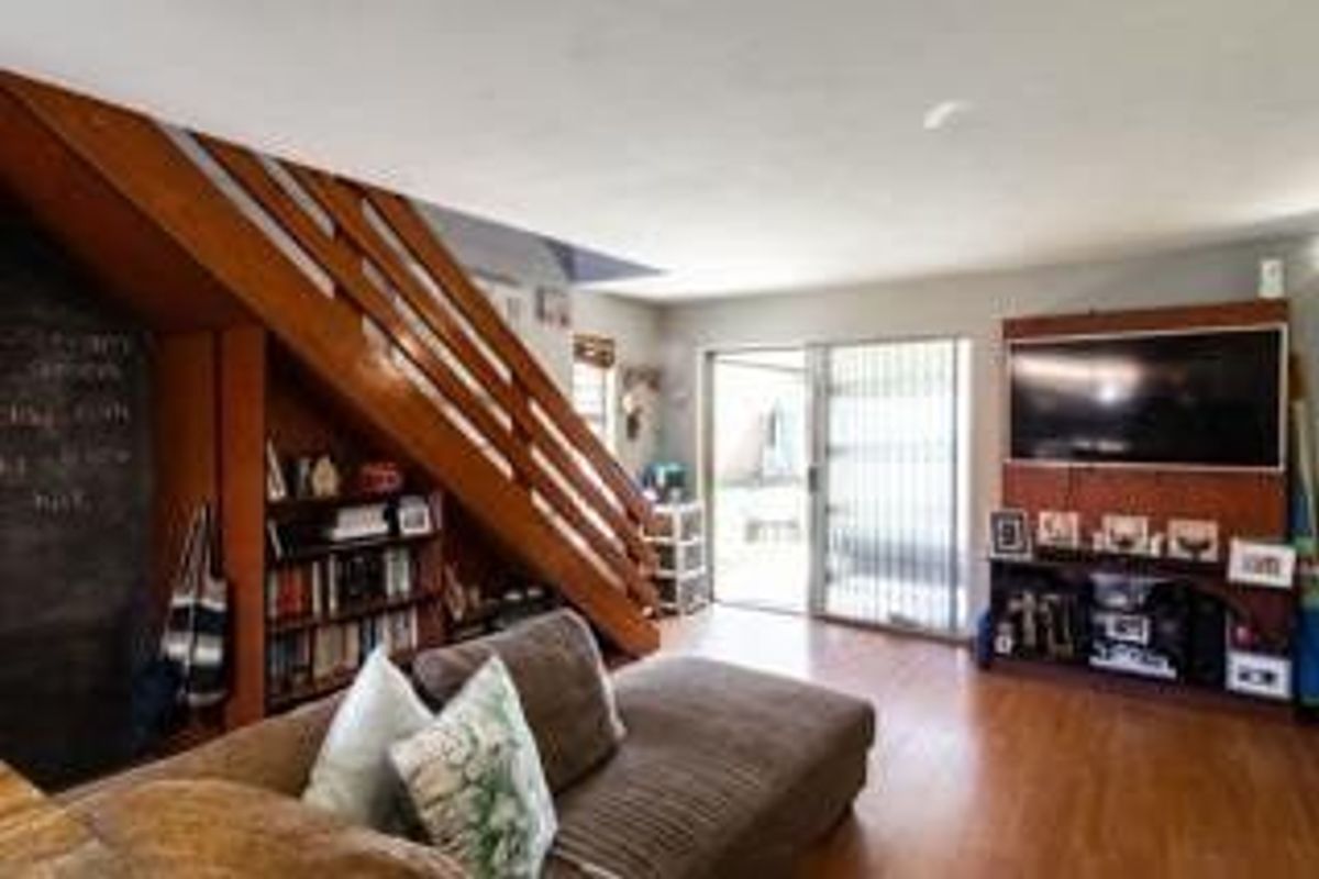 A living room featuring laminate flooring, a wooden staircase with integrated shelving, and a built-in media unit with access to an outdoor area.