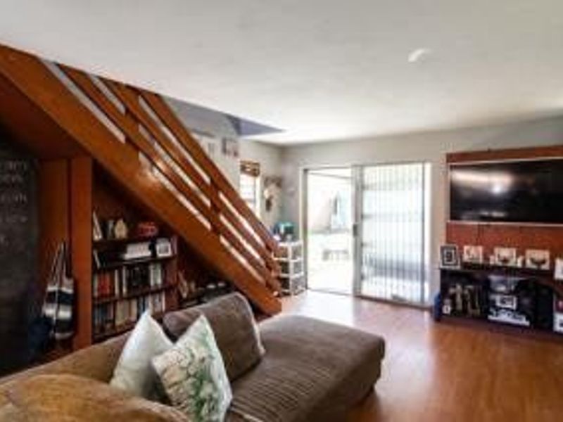 A living room featuring laminate flooring, a wooden staircase with integrated shelving, and a built-in media unit with access to an outdoor area.