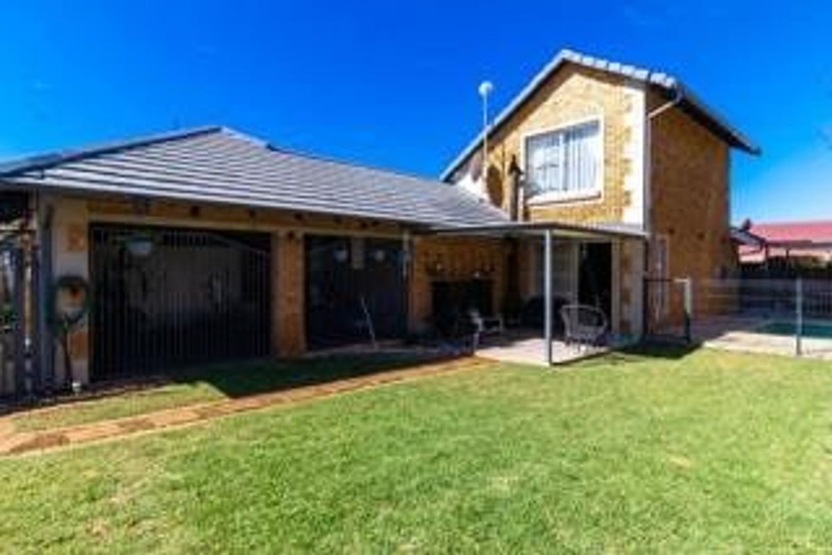 Rear view of the townhouse featuring a brick facade, tiled roof, and a covered patio area overlooking the private garden.