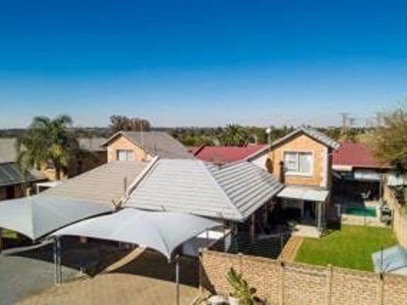 Aerial view of a townhouse property featuring a tiled roof, shade sail carport, paved driveway, and a private garden with a swimming pool.