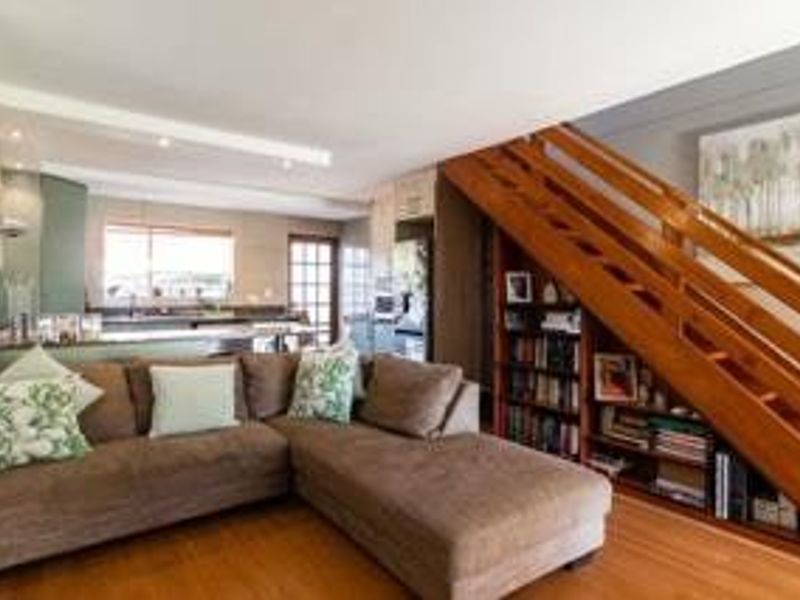 Open-plan living area featuring a wooden staircase with integrated shelving, flowing into a functional kitchen space with modern cabinetry and laminate flooring.