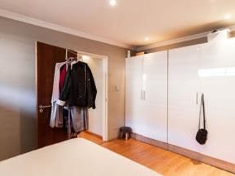 A well-maintained bedroom featuring modern white built-in cupboards, recessed downlighting, and warm laminate flooring.