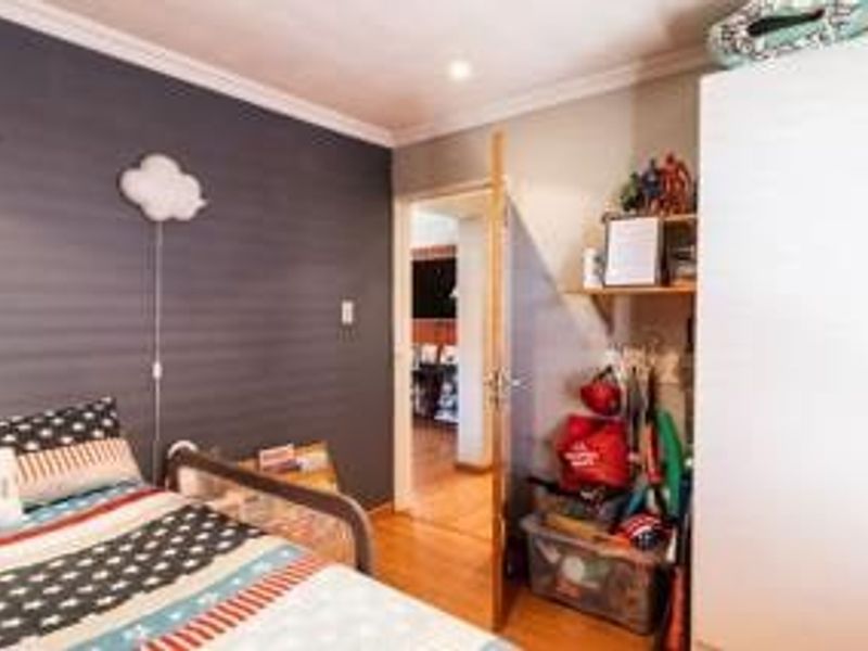 A bedroom featuring laminate flooring, a built-in wardrobe, and a dark accent wall, providing a functional space with potential for updated styling.
