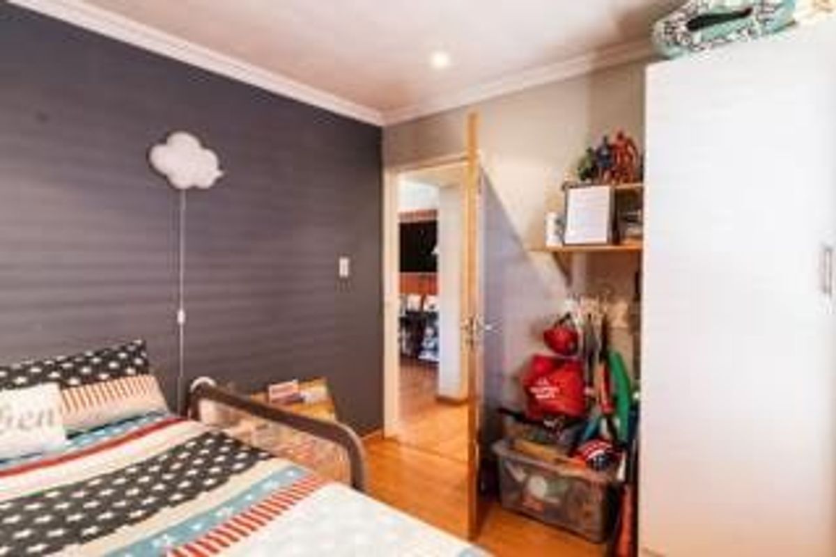 A bedroom featuring laminate flooring, a built-in wardrobe, and a dark accent wall, providing a functional space with potential for updated styling.