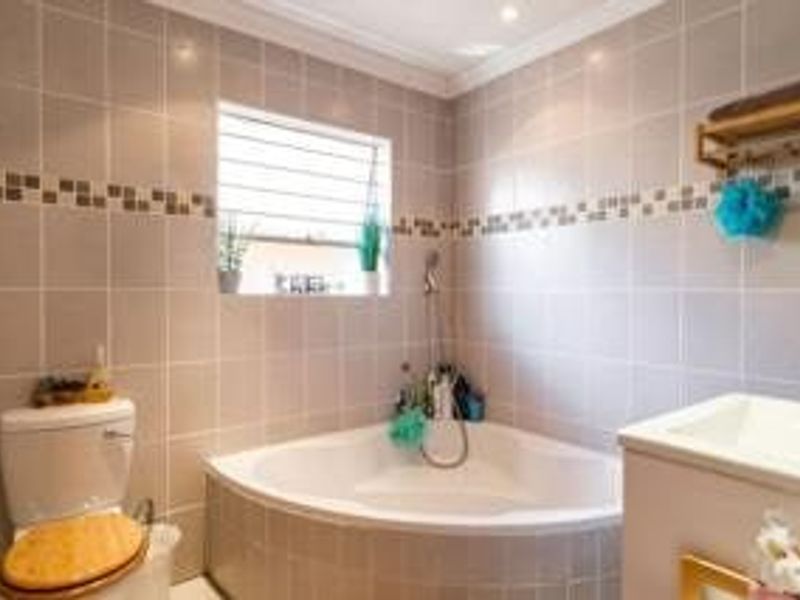 A functional bathroom featuring a corner bathtub, toilet, and vanity basin with neutral wall tiling and a window providing natural light.