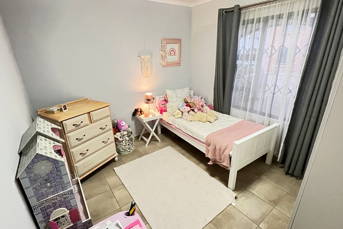 A functional bedroom featuring tiled flooring, a large window with security gate, and neutral wall finishes.