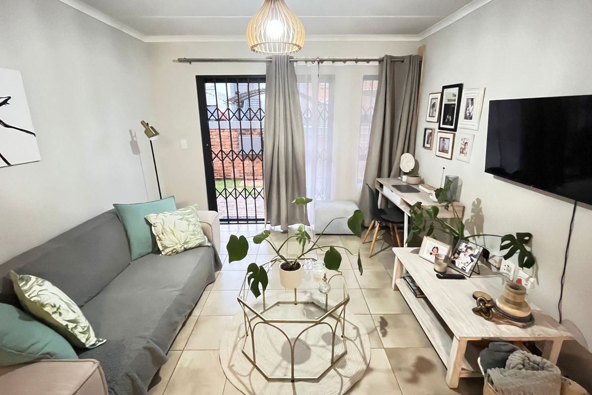 A well-maintained living room featuring tiled flooring and a security gate leading to an outdoor area, providing a bright and functional living space.