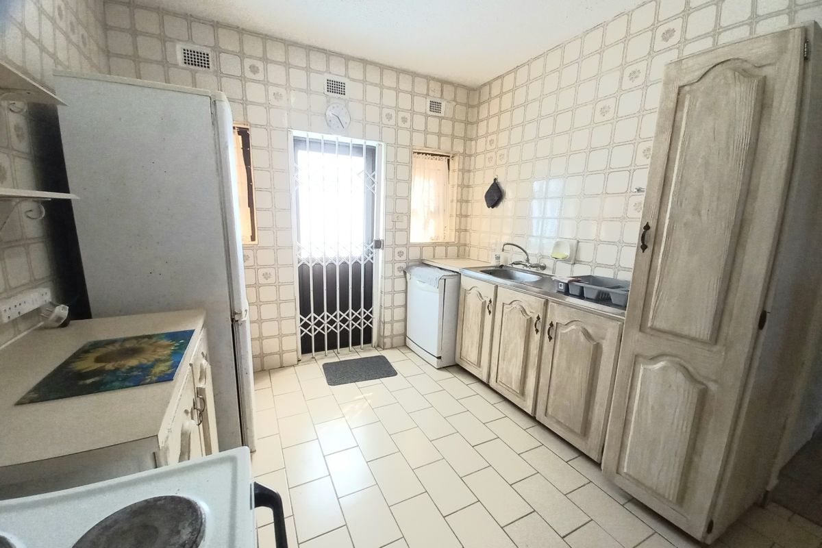 A functional kitchen featuring dated cabinetry, tiled walls and flooring, and a security gate leading to the exterior.