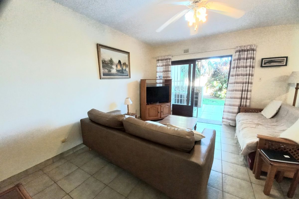 A living room featuring tiled flooring, a ceiling fan, and a sliding glass door providing direct access to the outdoor patio area.