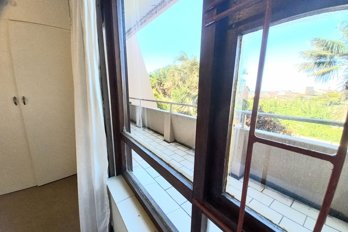 A bedroom featuring built-in cupboards and direct access to a tiled balcony with metal security bars and views of the surrounding area.
