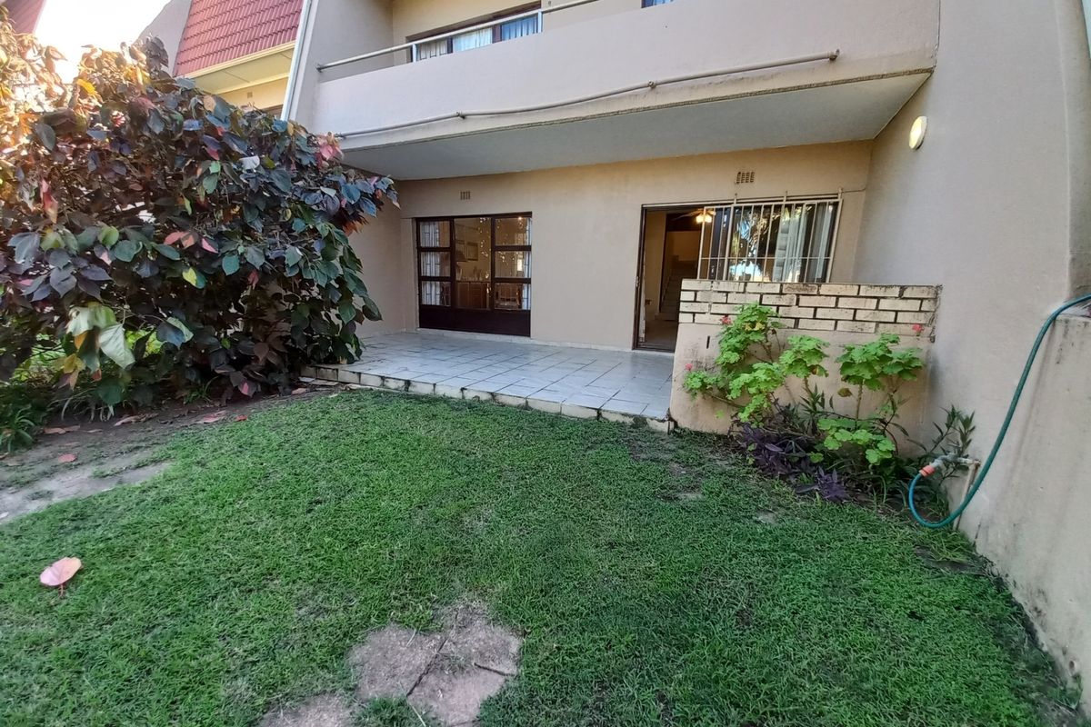 Rear view of the townhouse featuring a tiled patio area, a small private garden, and an upper-level balcony with sliding door access.