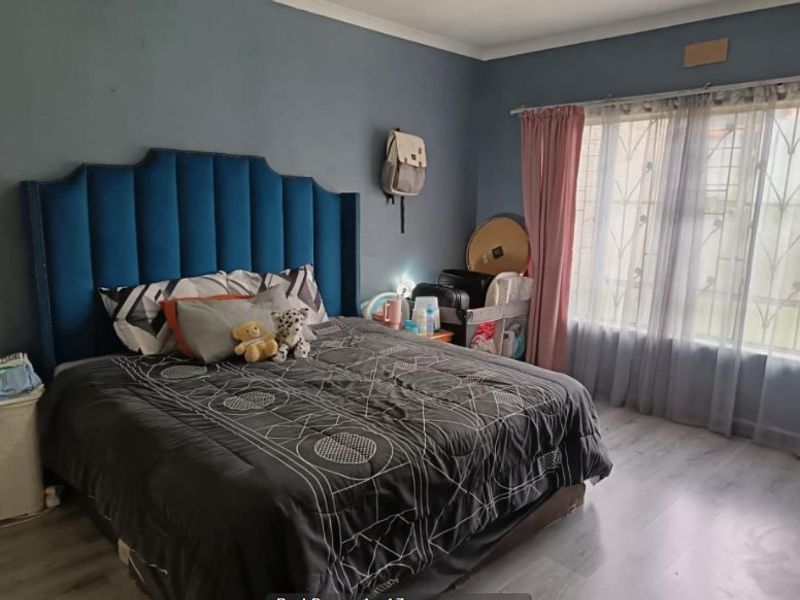 A spacious bedroom featuring laminate flooring and large windows fitted with security bars, providing natural light and a functional layout.