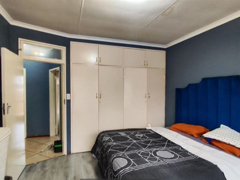 A bedroom featuring built-in cupboards, laminate flooring, and coved ceilings, providing a functional space with potential for cosmetic updates.