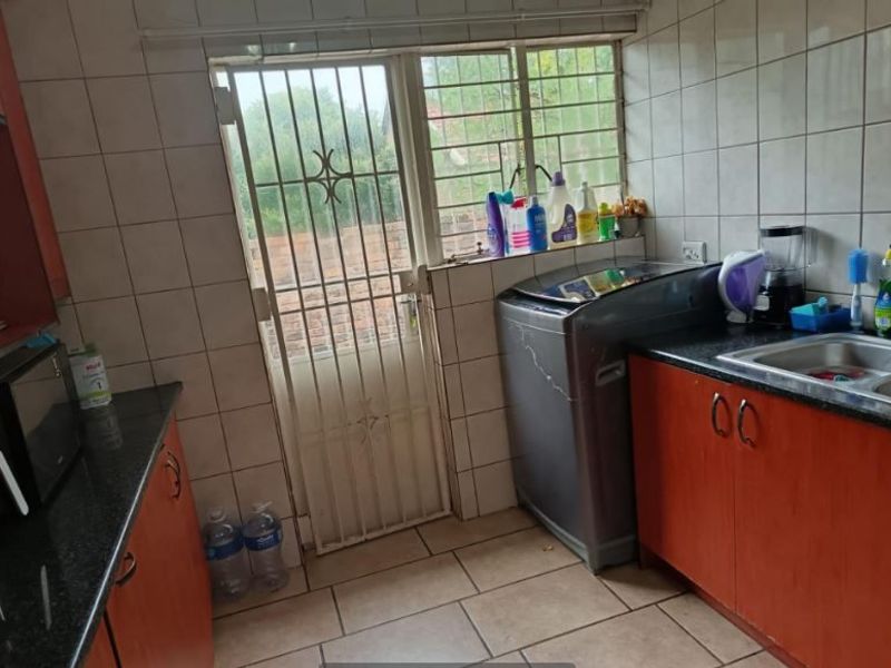 A functional laundry area featuring tiled walls, built-in cabinetry, laminate countertops, and a stainless steel sink with direct access to the exterior.