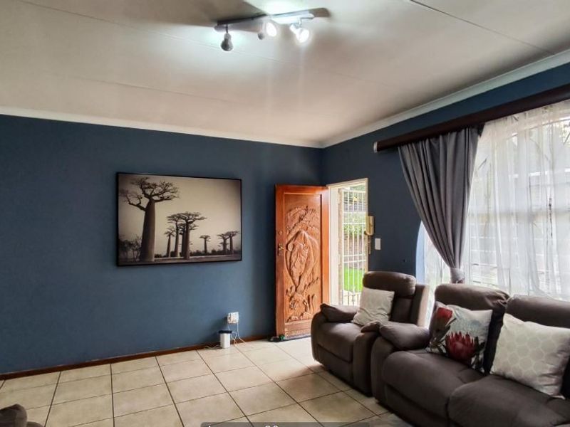 A living room featuring tiled flooring, a ceiling-mounted spotlight track, and a secure entrance door with an integrated security gate.